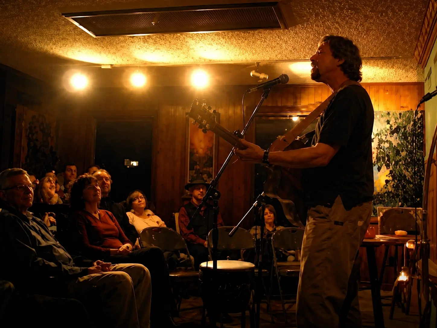 A performer singing at a microphone before an intimate audience in warm candlelit lighting